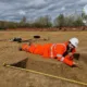 Reaching deep to retrieve some pottery and (inset) artist’s impression of the new police station at Milton. Dig photo: Archaeological Research Services Ltd